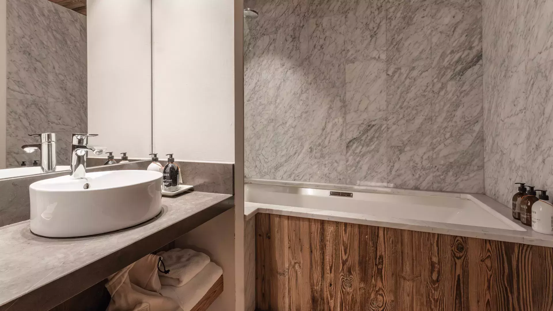 Salle de bain raffinée alliant murs en marbre blanc et baignoire habillée de bois vieilli au Penthouse Savoie.