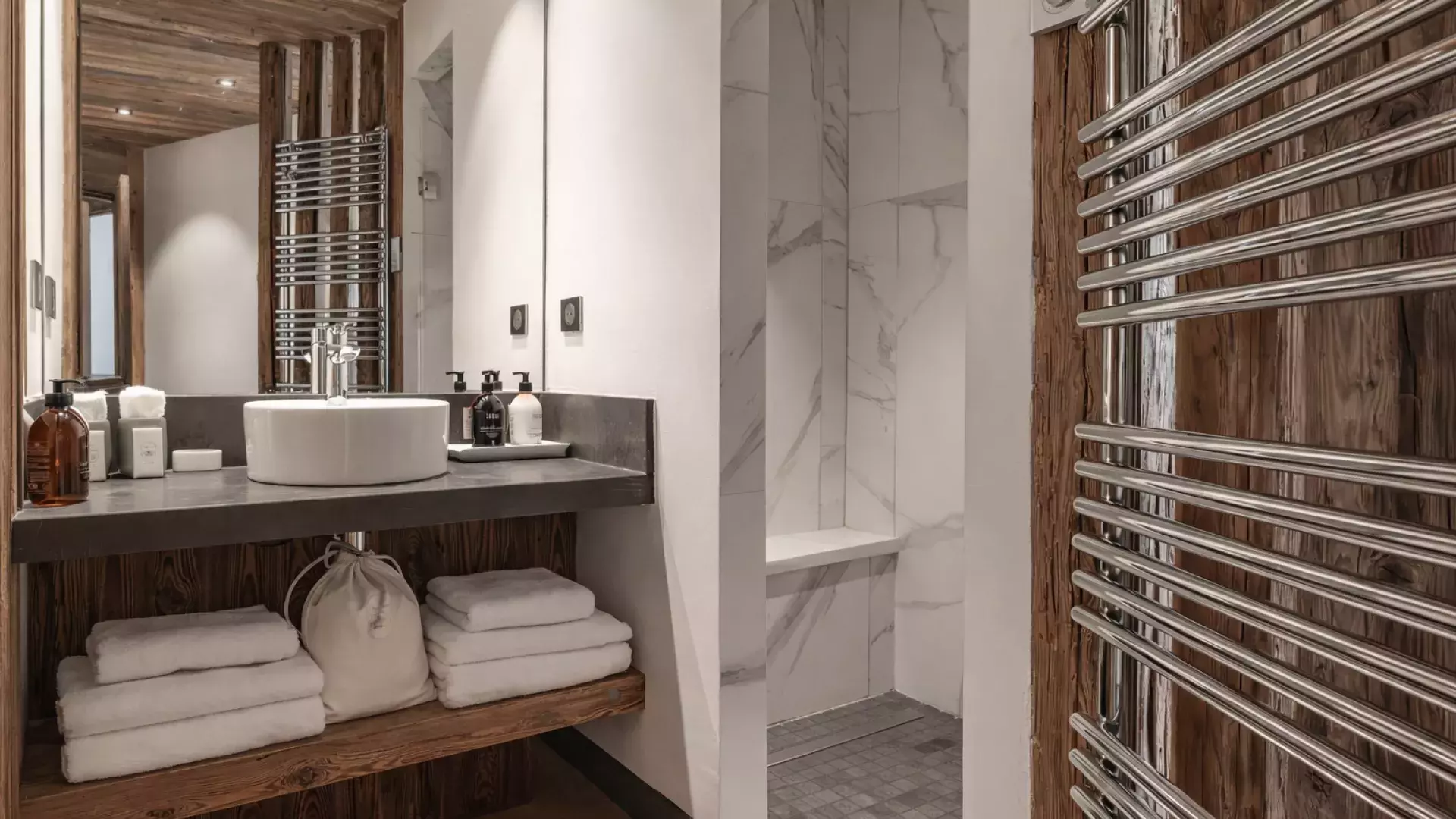 Salle de douche moderne avec douche à l'italienne en marbre, grand sèche-serviettes chromé et finitions bois au Penthouse Savoie.