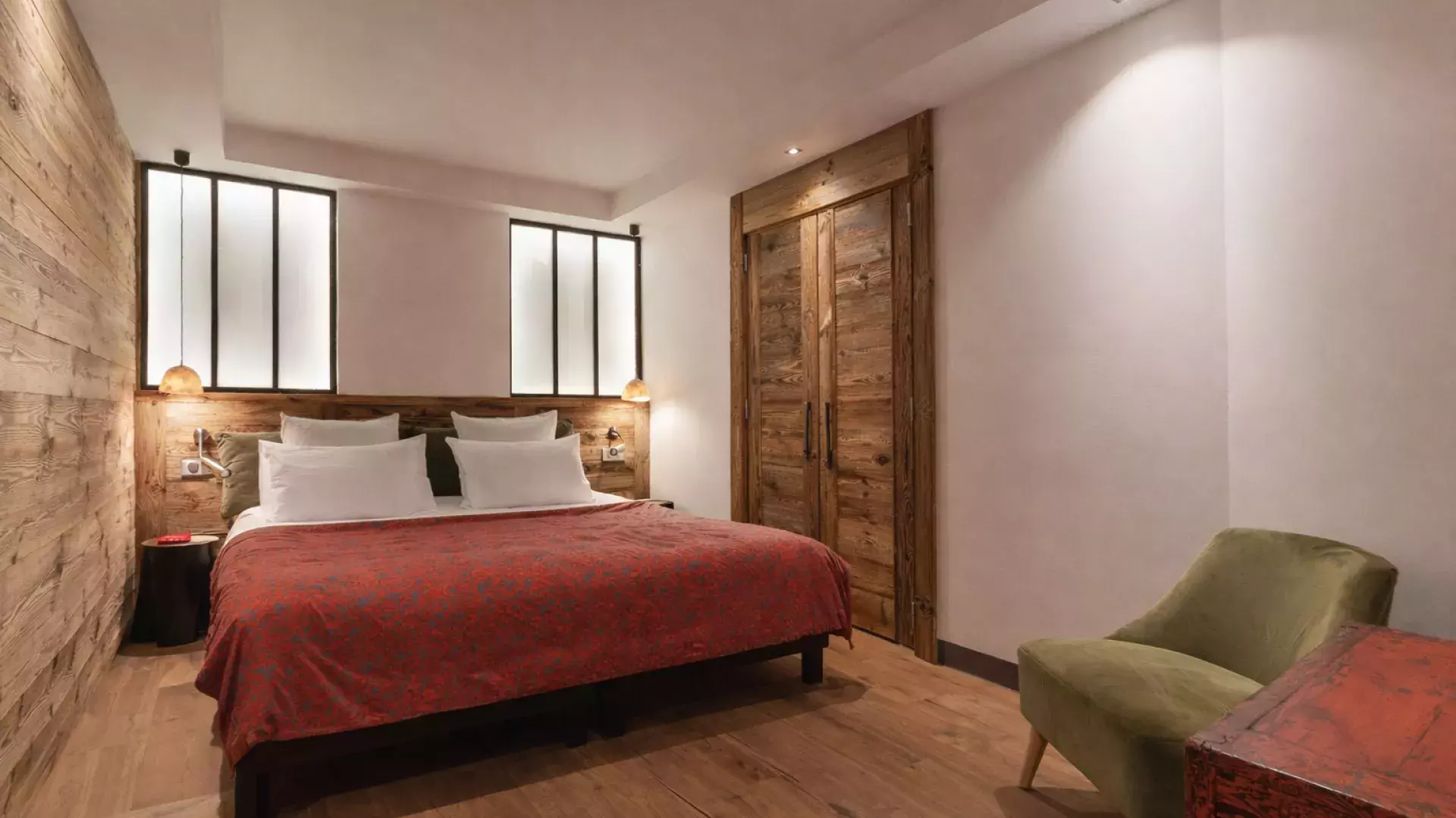 Chambre principale spacieuse aux accents rouges et verts, mêlant bois alpin et verrières style atelier au Penthouse Savoie.