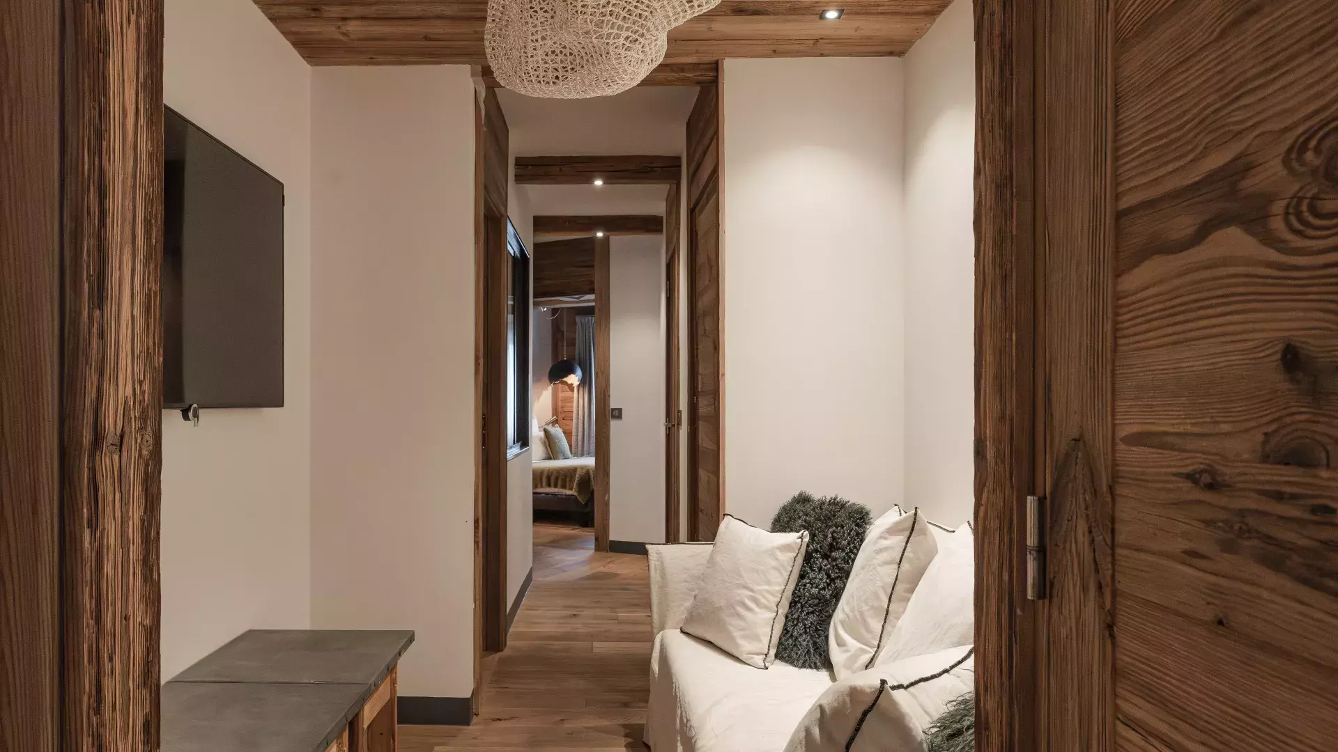 Dégagement de l'espace nuit aménagé en petit salon détente avec canapé blanc, TV murale et décoration boisée au Penthouse Savoie.