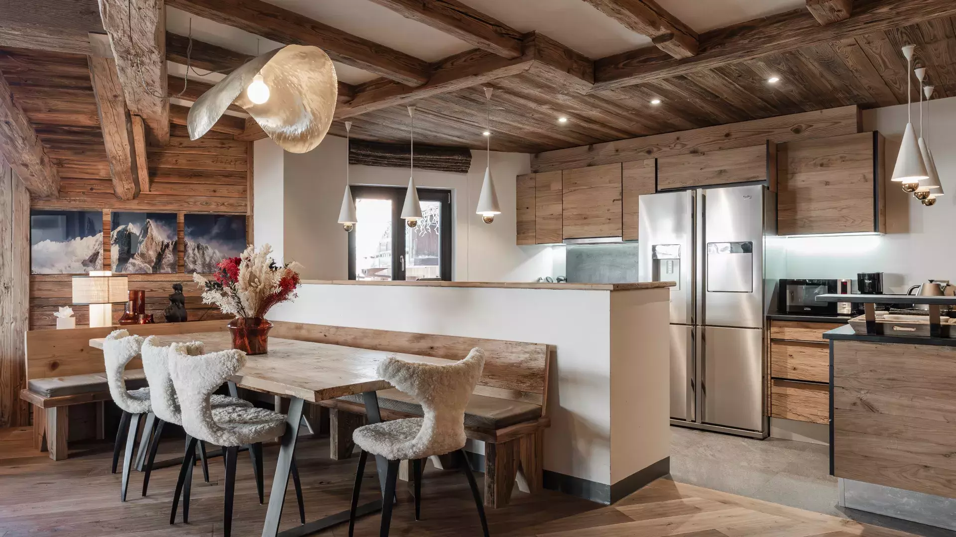 Espace salle à manger ouvert sur cuisine moderne avec table en bois massif, chaises en fourrure et suspensions design au Penthouse Savoie