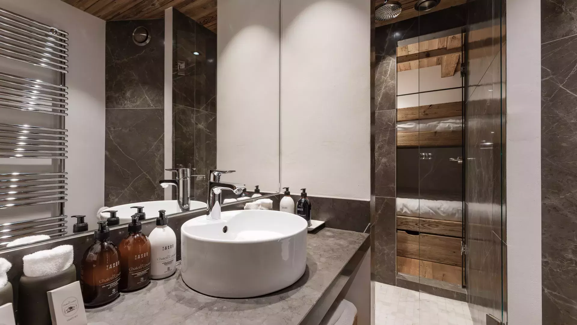 Salle de douche contemporaine en pierre sombre attenante au dortoir enfants (lits superposés visibles), équipée de produits d'accueil au Penthouse Savoie.