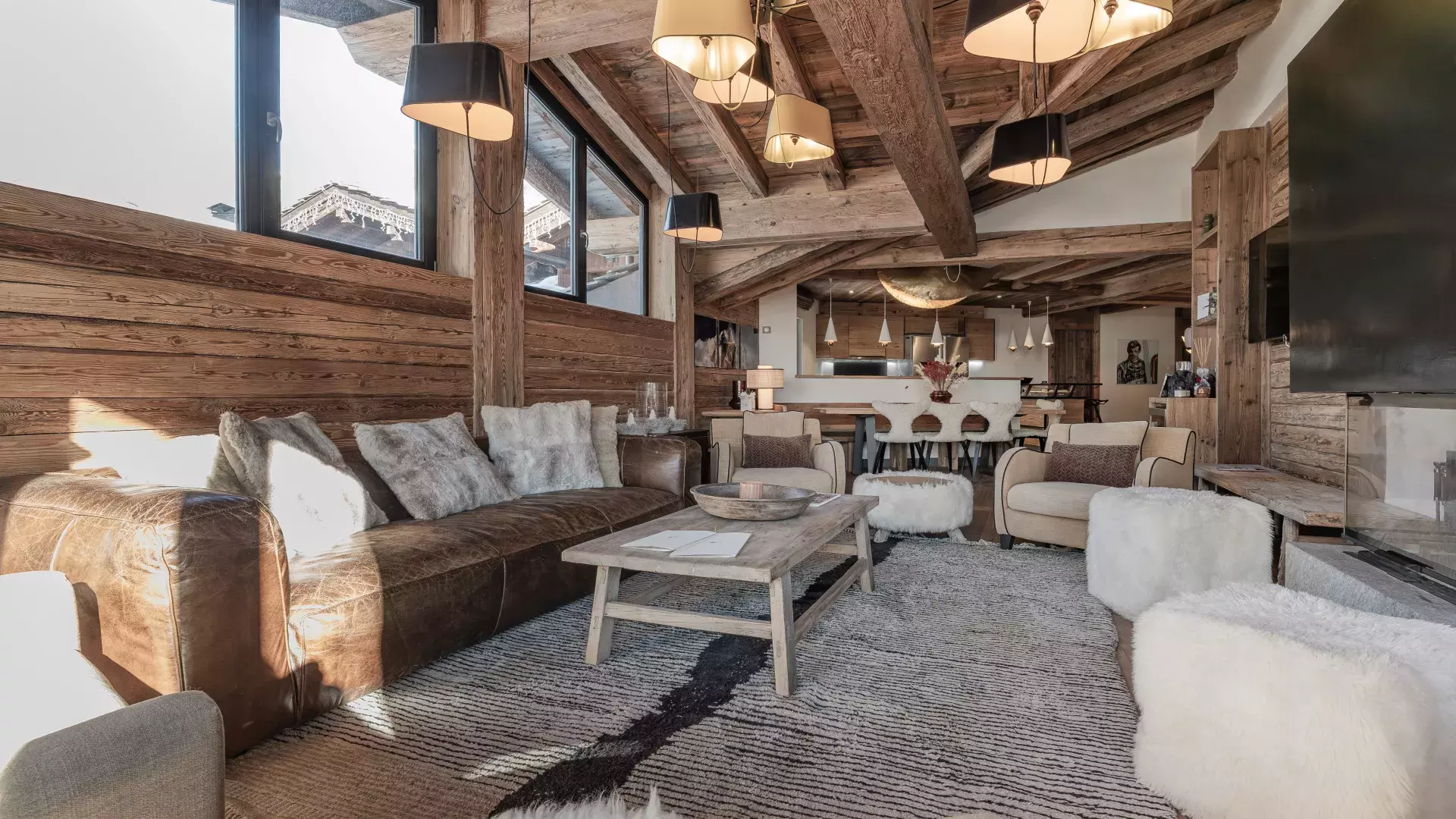 Grand salon baigné de lumière avec canapé en cuir vieilli, poufs en fourrure blanche et charpente apparente au Penthouse Savoie.