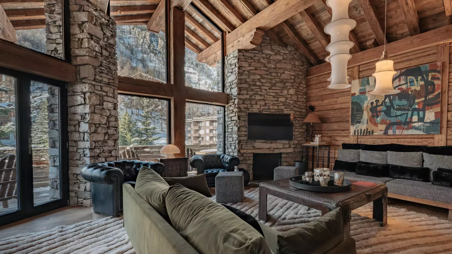 Grand salon cathédrale avec charpente apparente, canapés design en velours et cuir, et table basse coffre au Chalet Face.