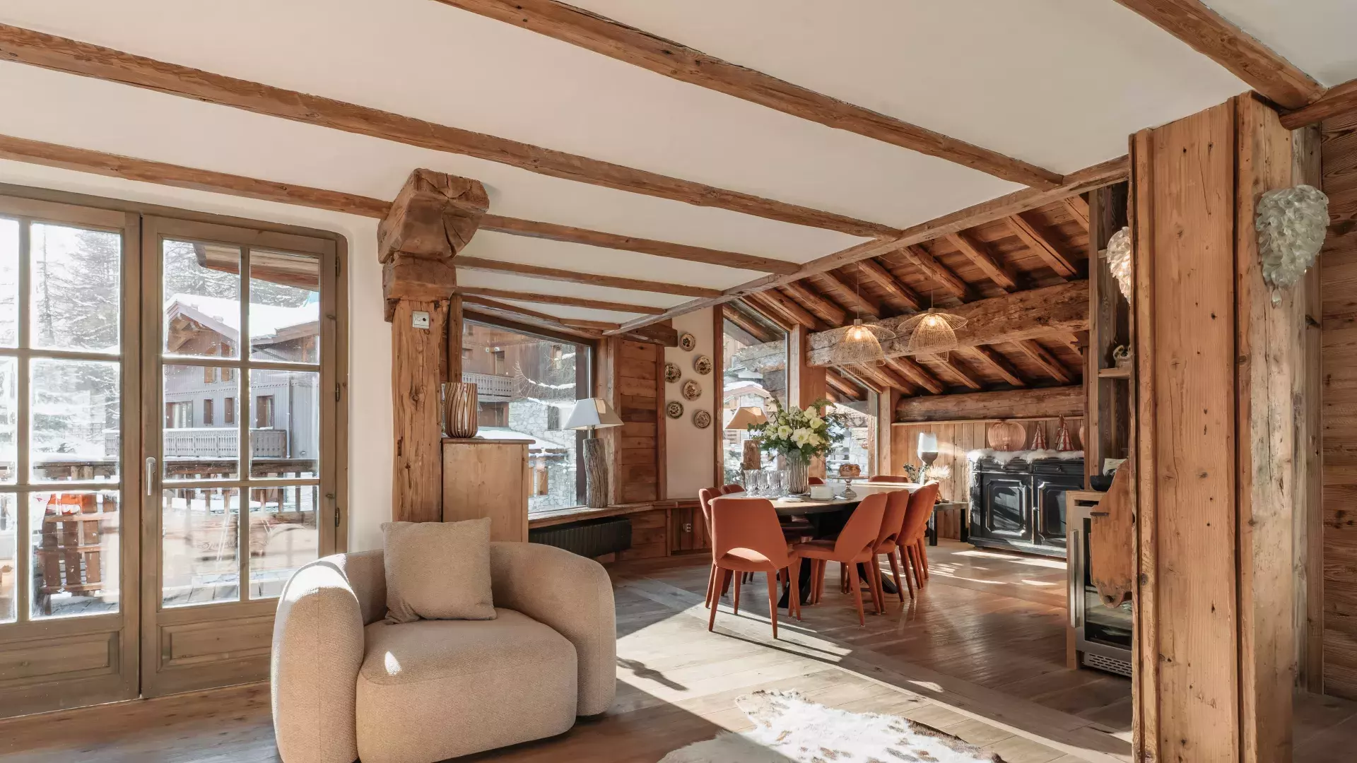 Espace de vie ensoleillé avec fauteuil design beige, tapis peau de vache et salle à manger chaleureuse sous charpente au Chalet Mathilda.
